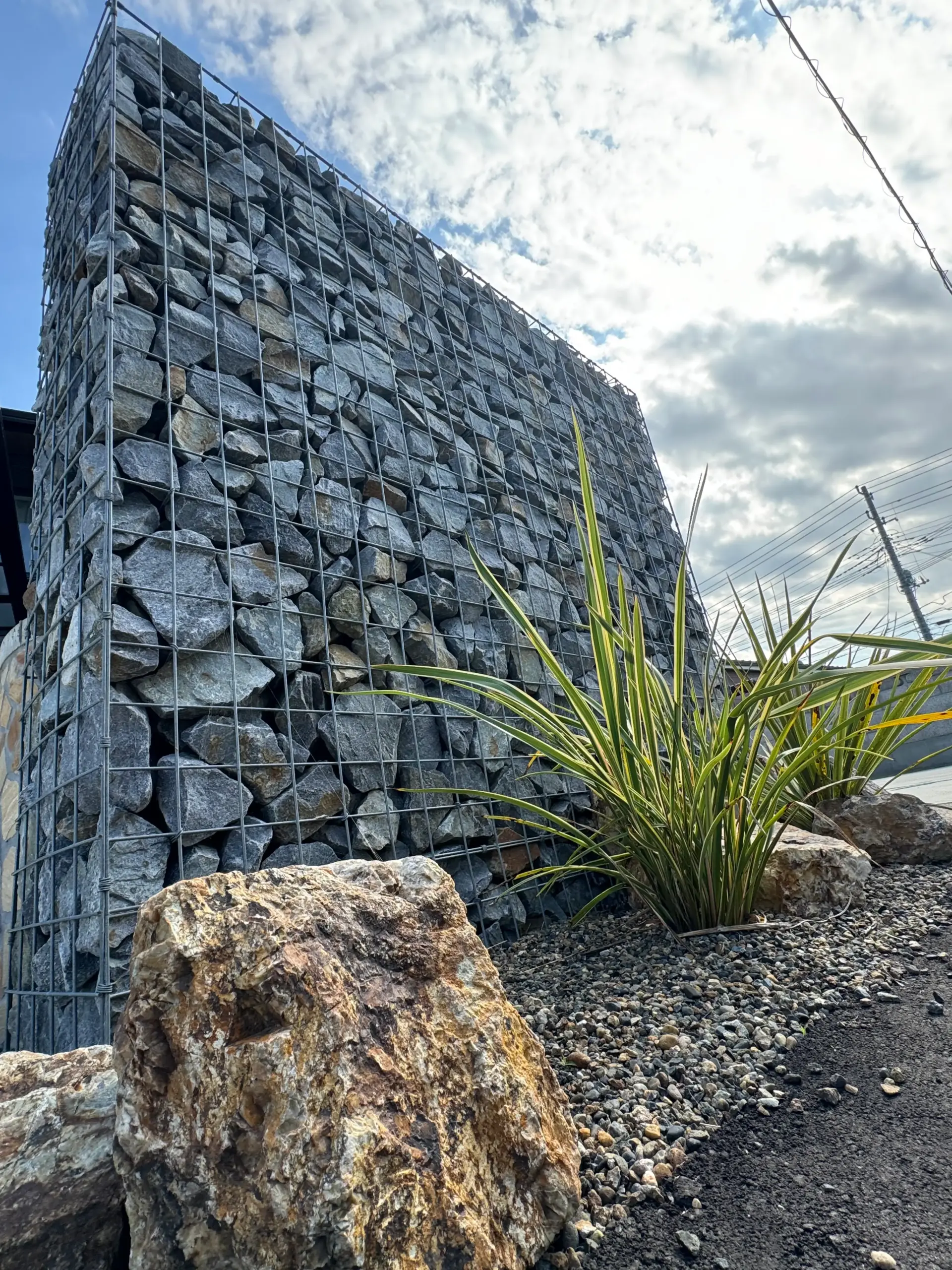 黒の天然石が詰まったガビオン門柱とドラセナのドライガーデン