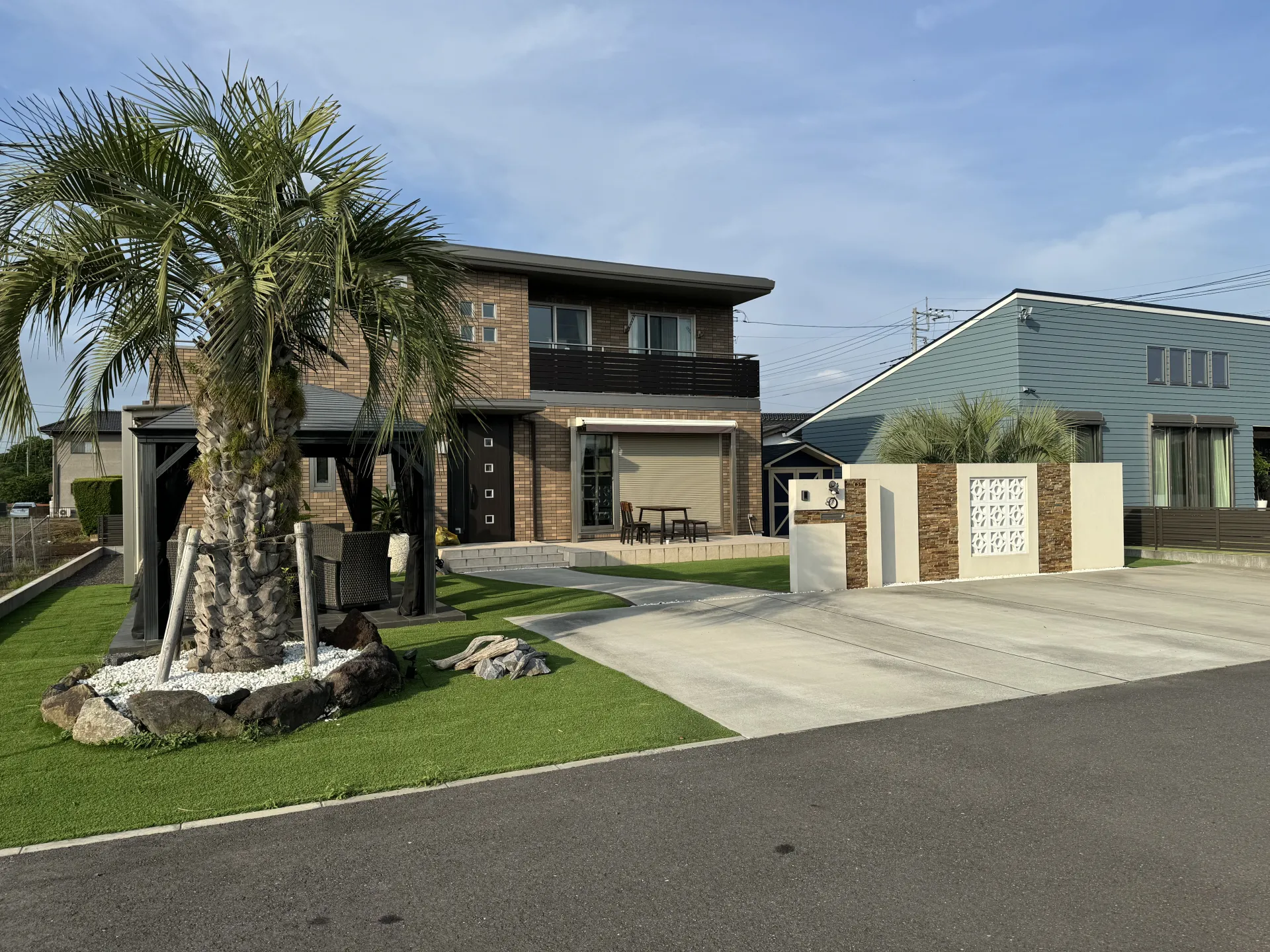 石岡市で施工した積水ハウスのリゾート風外構。やり替えた石貼り門柱と大きなデザイン門塀、ヤシの木の全景。